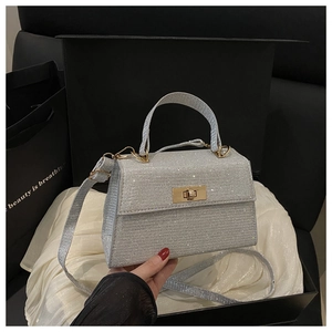 Detail of silver sequin handbag with gold turn-lock closure held by hand in gift box
