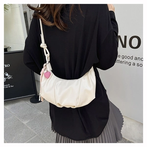 Detail of white crescent bag with pleats and pink heart charm in outdoor setting