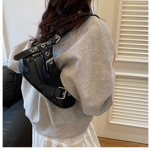 Detail of black patent leather saddle bag with silver buckles and punk eyelet design