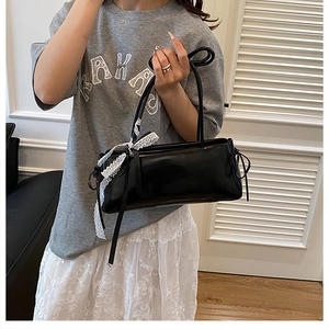 Détail du sac sous le bras en cuir noir avec un nœud en dentelle blanche et fini brillant