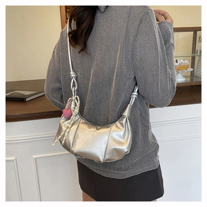 Detail of silver pleated crescent bag with pink heart charm shown on model in cafe