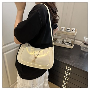 Detail of a creamy white glossy shoulder bag with metal buckle on a dark wood cabinet