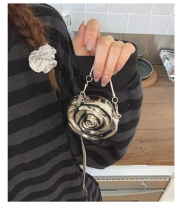Silver metallic rose-shaped evening clutch bag with chain strap held by hand