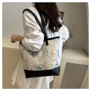 Dettaglio del ricamo floreale in pizzo e contrasto in pelle nera su una borsa tote