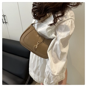 Detail of glossy khaki shoulder bag with gold metal hook clasp on white lace shirt