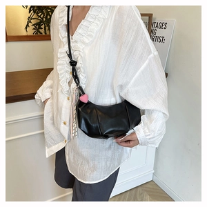 Detailed side view of black pleated crescent bag with pink heart and tassel charms