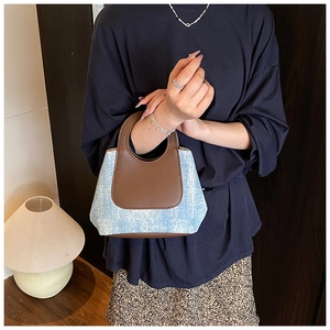Detail of vintage contrast stitching and brown leather handle on blue denim bucket bag