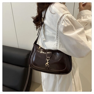 Detail of dark brown patent leather underarm bag with gold metal clasp on model