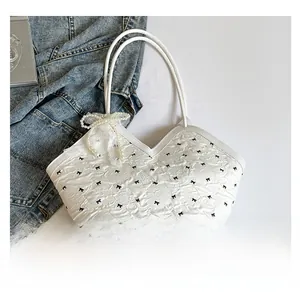 Detail view of white quilted tote bag featuring black bow prints and pearl lace charm