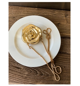 Detail of golden 3D rose acrylic evening bag with snake chain strap on white plate