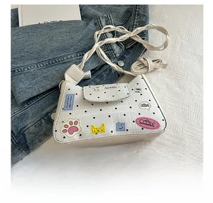 Detailed view of white polka dot shoulder bag with cartoon patches and phone for size comparison