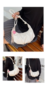 Close-up of beige crescent bag with pleated texture, knot strap and heart pendant detail