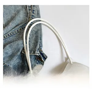 Detail of slim white handles and lace pearl bow decor on a textured tote bag