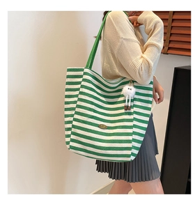Green and white striped canvas tote bag detail showing metal logo and plush pendant