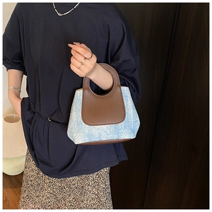 Dettaglio del tessuto denim a contrasto e manico in pelle marrone su borsa a secchiello