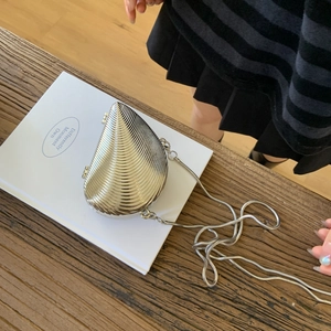 Sac de soirée argenté en forme de coquille avec bandoulière chaîne sur un livre