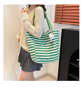 Close-up of green and white striped canvas tote bag with a plush ball charm and handmade tag