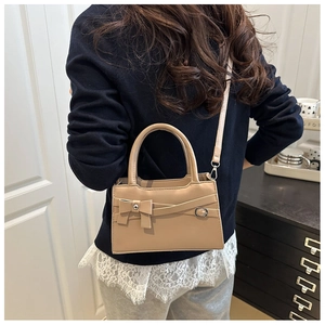 Sac à bandoulière beige chic avec nœud, porté à l'épaule dans un décor intérieur élégant