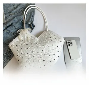 Detail of white bucket bag with black bow print, pearl lace charm and logo patch