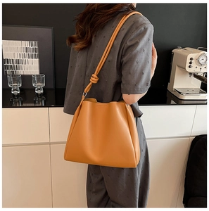Detail of a ginger yellow bucket bag with a stylish knotted shoulder strap on a model