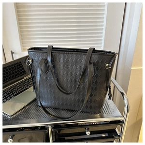 Close-up of black quilted tote bag with metal eyelet detail and long shoulder straps
