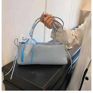 Détail du sac sous le bras bleu clair brillant avec nœud en dentelle et poignées fines