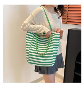 Close-up of green and white striped canvas tote bag with metal emblem and shoulder strap