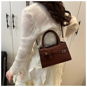 Détail du sac à main marron avec nœud décoratif et boucle en métal porté par le mannequin