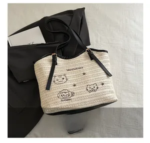 Detail of woven straw tote bag featuring cat embroidery and adjustable black leather straps