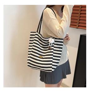Detailed side view of large striped canvas tote bag with cute plush pendant and gold label
