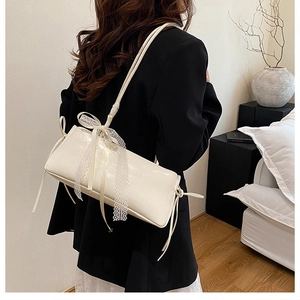 Détail du sac à bandoulière en cuir verni blanc crème avec nœud décoratif en dentelle