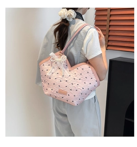 Detail of pink heart-shaped tote bag with black bow prints and pearl charm on model