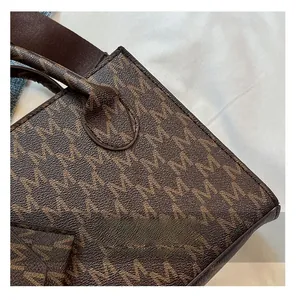 Detail of brown tote bag featuring M-letter monogram print and wide fabric shoulder strap