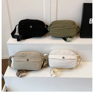 Four lightweight nylon crossbody bags in black, green, khaki, and cream on a white stand