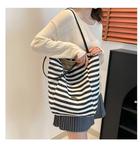 Detail of large black and white striped tote bag with leather strap and metal logo