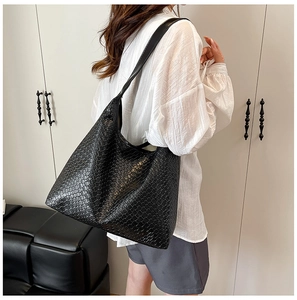 Detail of a large black woven PU leather tote bag shown on a model's shoulder