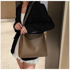 Détail du sac cabas en cuir mat marron foncé porté par un mannequin dans un décor moderne