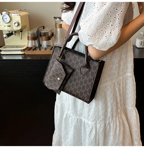 Borsa tote marrone monogramma con manici e pochette su sfondo di abito in pizzo bianco