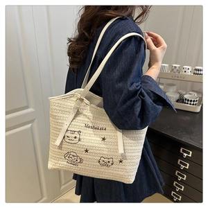 Detail of hand-woven straw tote with white leather strap and cat embroidery pattern