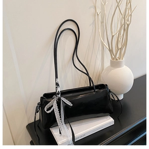 Détail du sac sous le bras en cuir noir brillant avec un nœud en dentelle blanche