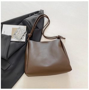 Detail of a brown leather tote bag with unique spiral knotted strap design and stitching