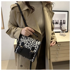 Detail of leopard print crossbody bag with black trim and gold hardware on trench coat