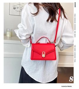 Détail du sac carré en cuir rouge avec poignée métallique et fermoir porté par un mannequin