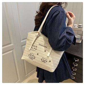 Detail of cream straw tote bag featuring cartoon cat embroidery and adjustable leather strap