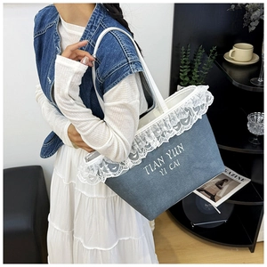 Detail of blue denim tote bag with white lace trim and branded lettering on the surface