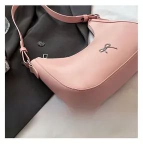Detail of pink crescent bag featuring silver bow metal ornament on grey fabric