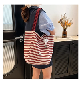 Macro detail of red and white striped canvas tote bag with soft plush monster pendant charm