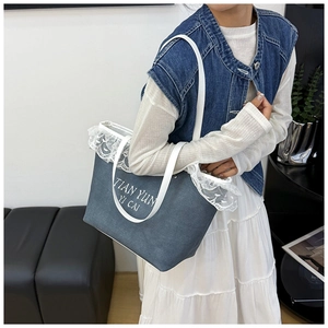 Detail of blue denim tote bag featuring white lace trim and embroidered lettering