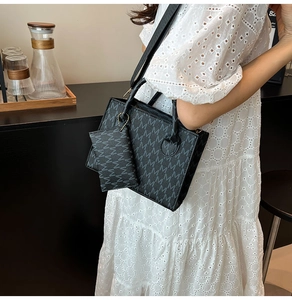 Detail of a black patterned tote bag set with wide shoulder strap on a white dress model