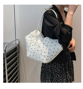 Detailed view of a white tote bag with black bows and a pearl bow charm on a model